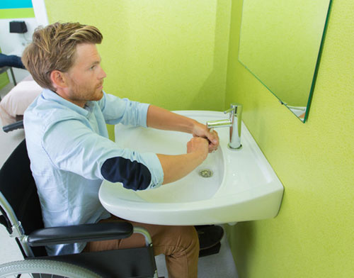 Mann im Rollstuhl sitzt vor einem Waschbecken